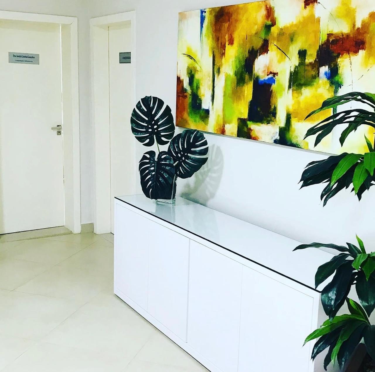 Corredor de acesso aos consultórios da Clínica Raphael, com aparador branco e obra de arte na parede