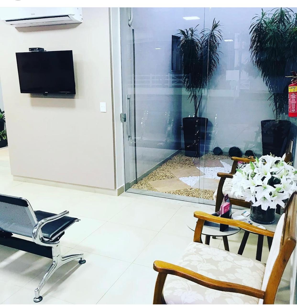Área de espera da Clínica Raphael com jardim de inverno atrás de painel de vidro