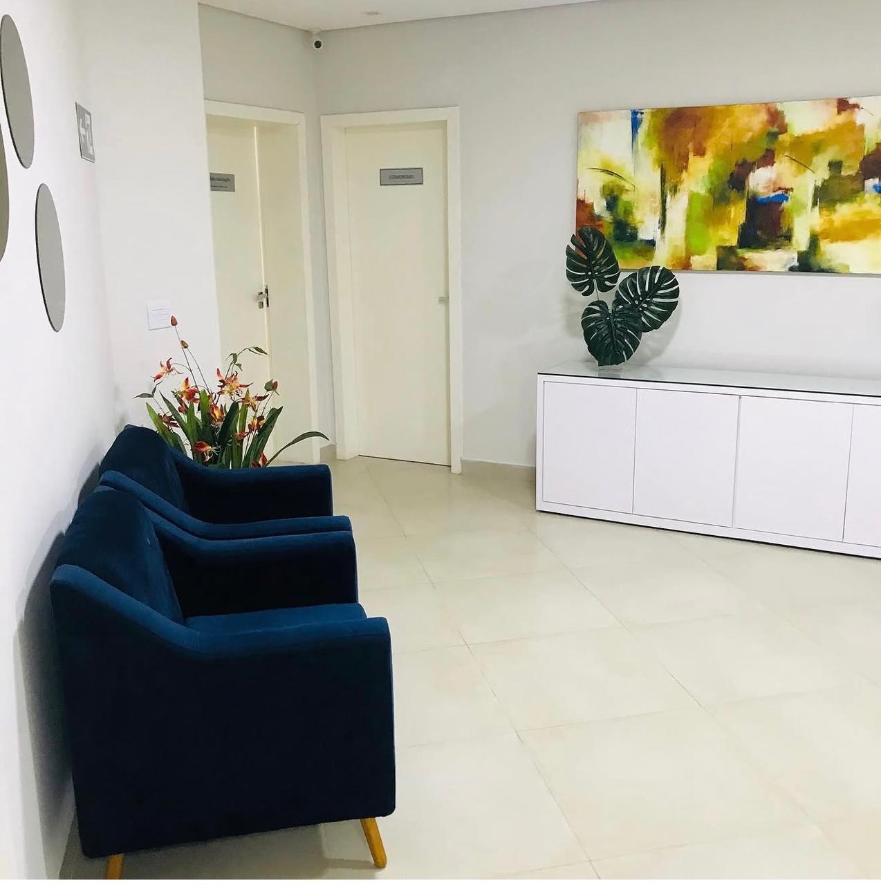 Sala de espera da Clínica Raphael, com poltronas azuis, ambiente claro e arranjo de flores
